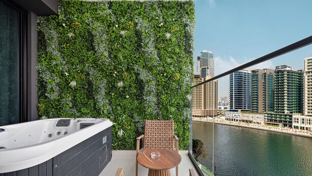 A balcony with a hot tub, wooden furniture, and a lush vertical garden wall.