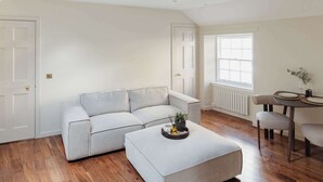 A modern living room with a sectional sofa, a small table with chairs, and a large window providing natural light. - Charming Central Mews Home with Secure Parking (Edinburgh)