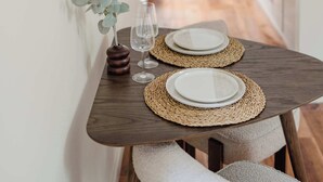 A dining table with two plates and wine glasses, set with woven placemats, in a narrow kitchen with wooden flooring and white cabinets. - Charming Central Mews Home with Secure Parking (Edinburgh)