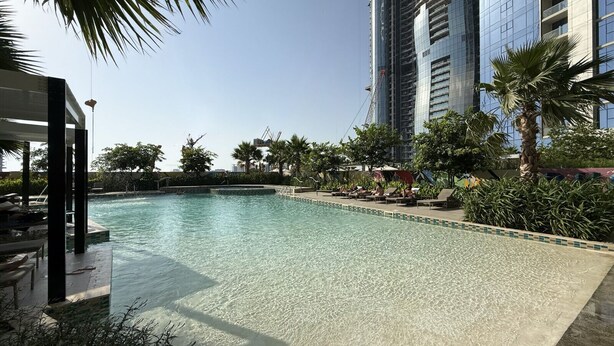 Ein Swimmingpool mit Liegestühlen und Palmen, umgeben von Hochhäusern.