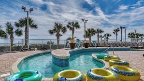 Piscina con varios flotadores, palmeras y sillas de descanso.