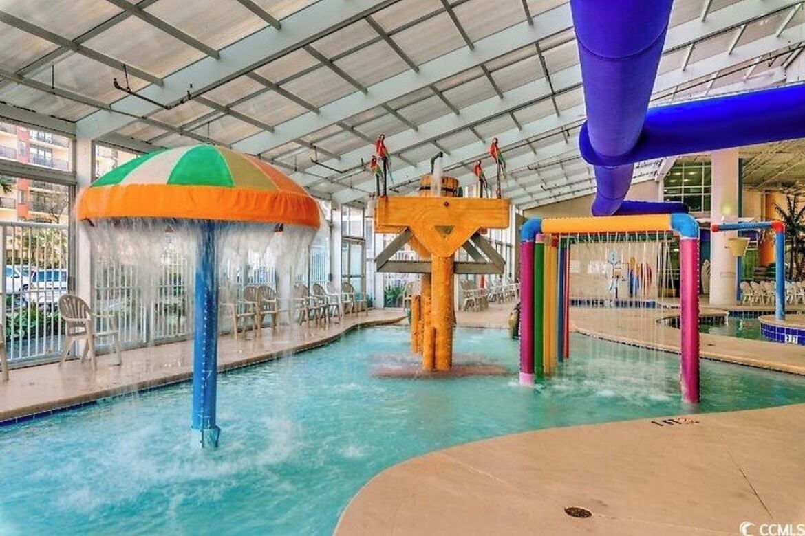 An indoor water park with a large pool, water slides, and a colorful umbrella structure.