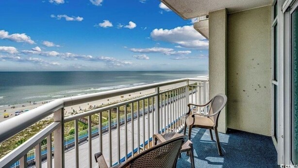 Un balcón con vista a la playa y al océano, una silla y una mesa.