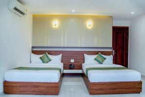 Een tweepersoonskamer met twee bedden, een houten hoofdbord, een wandairconditioner en een deur.