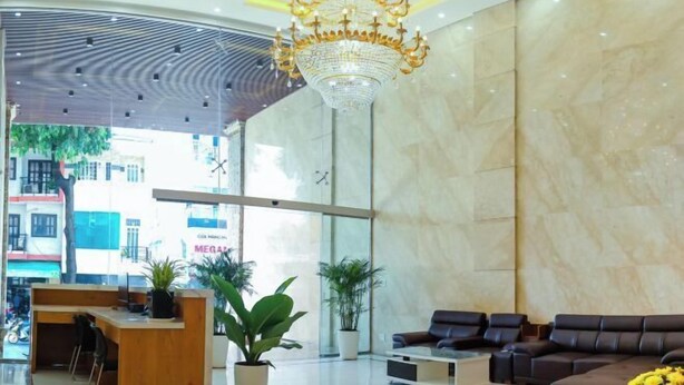 Een moderne hotel lobby met een grote kroonluchter, een zithoek, een receptiebalie en potplanten.