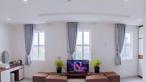 Een moderne woonkamer met een flatscreen televisie, twee potplanten, een bank en een bureau met een spiegel.