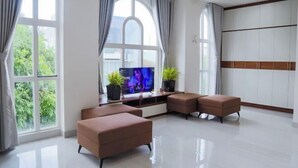 Een moderne woonkamer met een flatscreen televisie, twee potplanten en een groot raam met gordijnen.