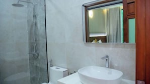 Een badkamer met een douche met glazen wand, een witte wastafel en een spiegel erboven.