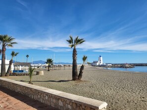 A beach with palm trees, a lighthouse, and boats in the background.