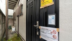 Une ruelle étroite, avec un portail noir, un panneau jaune interdisant tout dépôt d’objets et un panneau d’affichage sur lequel sont accrochés divers avis.