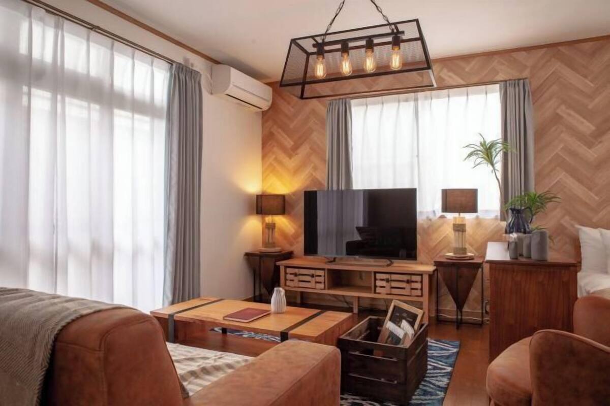 A modern living room with a flat-screen TV, wooden furniture, and a herringbone-patterned wall.