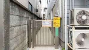 Une ruelle étroite, avec un portail en métal, des unités de climatisation et un panneau indiquant qu’il est interdit de fumer.