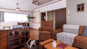 Un salon comprenant un canapé, un fauteuil, un meuble en bois et une table sur laquelle se trouvent un vase et un livre.