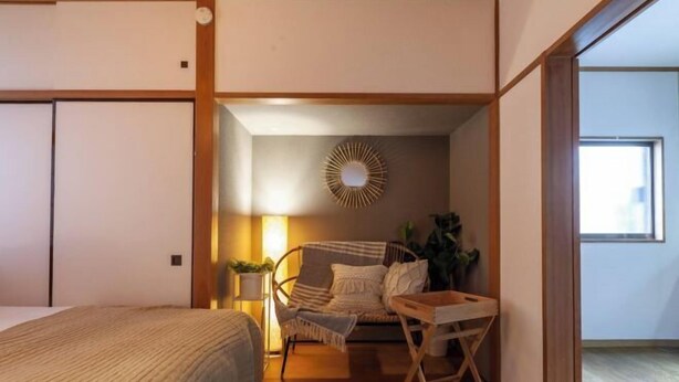 Une chambre à coucher comprenant un lit, une chaise, une petite table, un luminaire fixé au mur et un élément décoratif mural.