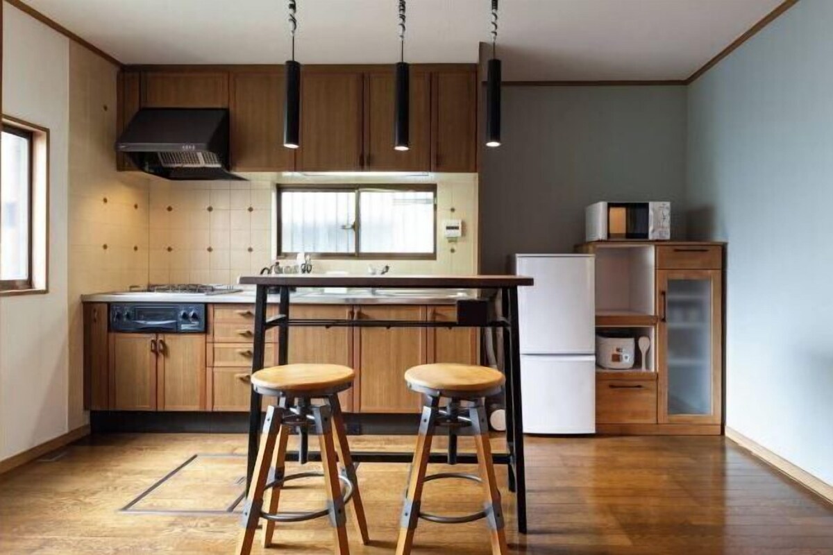A kitchen with wooden cabinets, a central island with stools, pendant lighting, and a refrigerator.