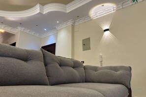 Una sala de estar moderna con un sofá grande de color gris, iluminación empotrada en el techo y un aplique de pared.