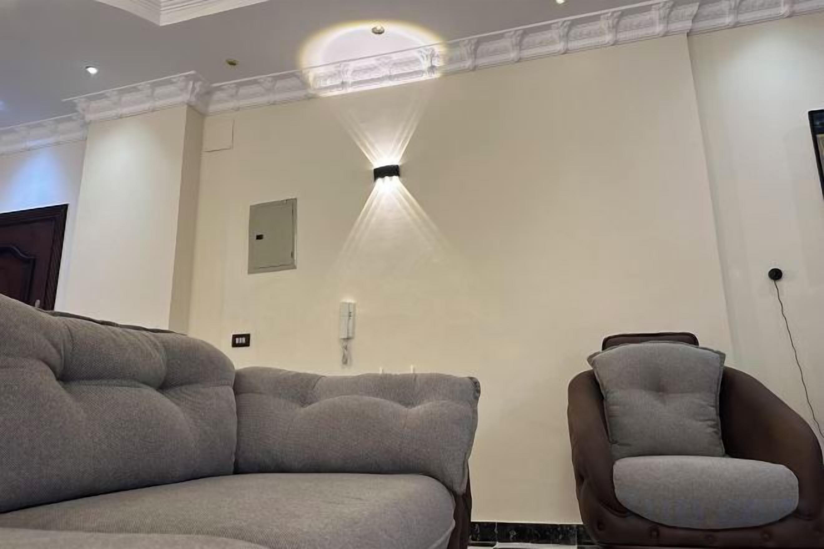 A room with a large grey sofa, a smaller armchair, and a wall-mounted light fixture.