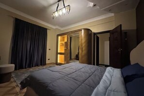A hotel room with a large bed, a seating area with a chair, a wardrobe, and a mirror. - Chessboard Oasis - Elite 2BR apart by BC residence (New Cairo City)