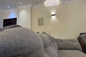 A room with a grey sofa, a wall-mounted light fixture, and a door. - Chessboard Oasis - Elite 2BR apart by BC residence (New Cairo City)