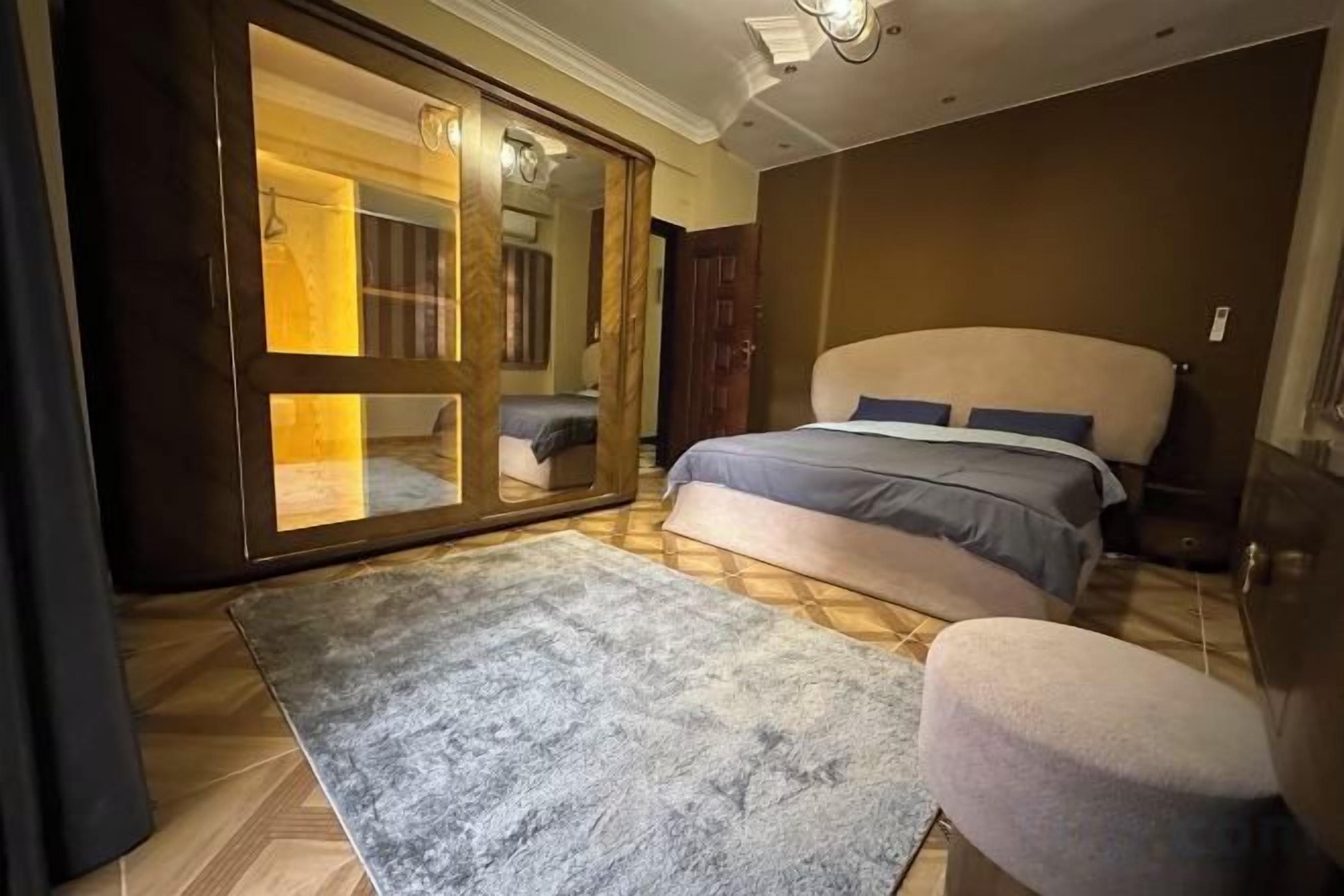 A bedroom with a bed, a large mirror, a wardrobe, and a small stool.