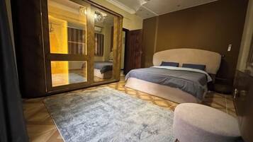 A bedroom with a bed, a large mirror, a wardrobe, and a small stool.