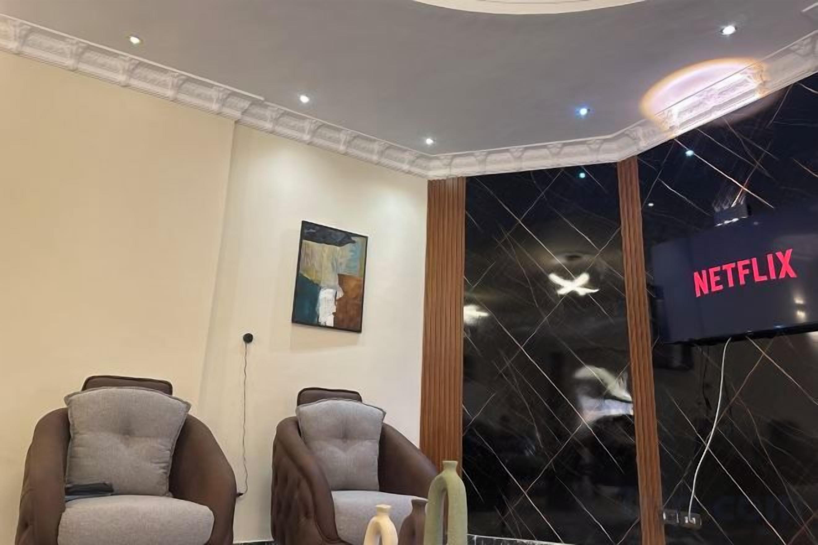 A room with two armchairs, a wall-mounted artwork, a window with a view of the night sky, and a sign indicating a Netflix service.