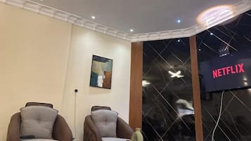 A room with two armchairs, a wall-mounted artwork, a window with a view of the night sky, and a sign indicating a Netflix service.