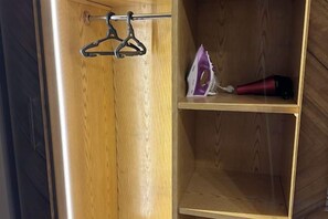 A wooden wardrobe with a hanging rod and a shelf with a hairdryer. - Chessboard Oasis - Elite 2BR apart by BC residence (New Cairo City)