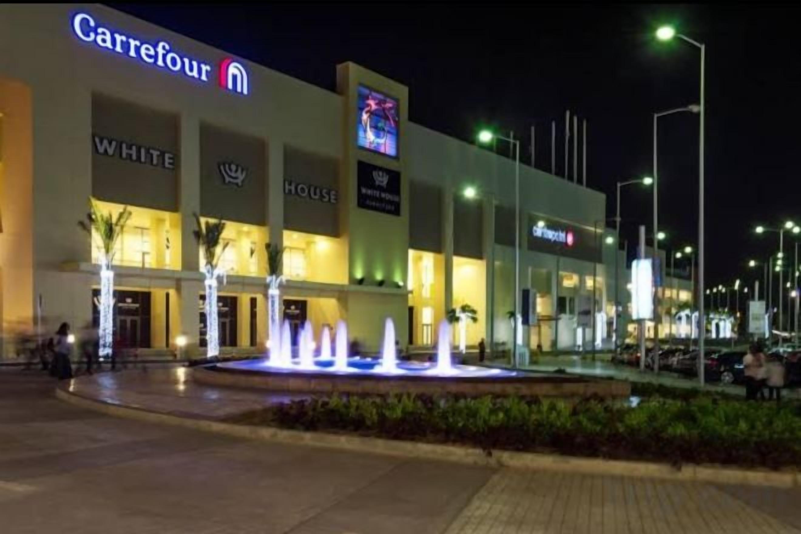 A Carrefour store at night with a fountain in front.