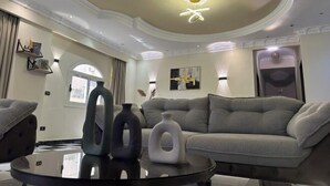 A modern living room with a grey sofa, a round coffee table, and decorative vases. - Chessboard Oasis - Elite 2BR apart by BC residence (New Cairo City)