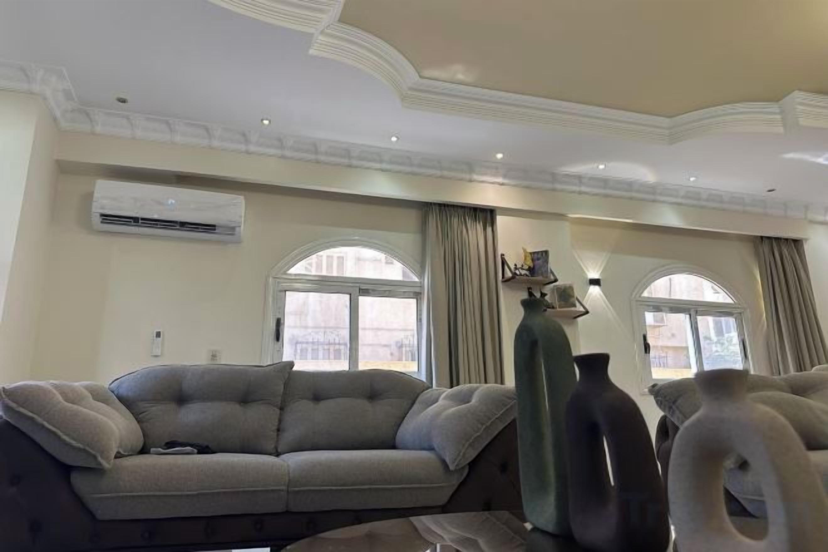 A living room with a sofa, a large vase, and a window with curtains.