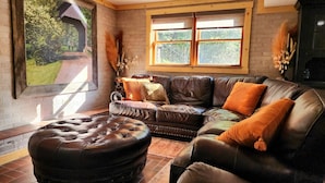 A cozy living room with a leather sofa, ottoman, and a large window providing a view of greenery.