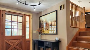 A wooden door, a painting, a vase with flowers, a black desk, and a staircase.