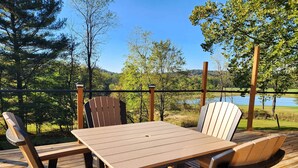 A wooden deck with a table and chairs, overlooking a lake and forest.