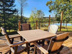 Une terrasse en bois avec une table et des chaises, donnant sur un lac et une forêt.