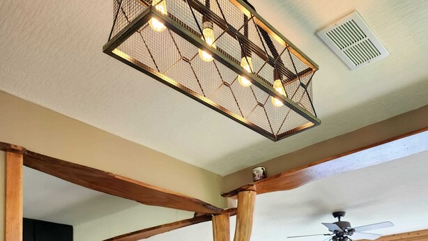 A spacious dining area with a wooden table set for a meal, a ceiling fan, and a view of the kitchen and living room in the background.