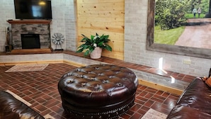A cozy living room with a stone fireplace, a large TV, and a wooden wall.