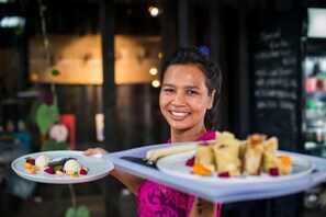 A person holding a tray with two plates of food, one with dumplings and the other with pastries, in a restaurant setting.