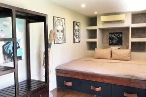 A bedroom with a bed, a wooden wardrobe, and artwork on the walls.