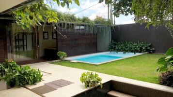 A backyard with a swimming pool, a wooden deck, and potted plants.