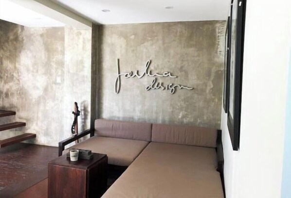 A modern living room with a large sectional sofa, a wooden coffee table, and a concrete accent wall with a 'furniture design' sign.
