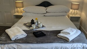 A neatly made bed with white linens, a tray with cups and a flower, and towels on the side.
