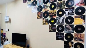 A room with a wall decorated with vinyl records and album covers, a television, and a wooden cabinet. - Kulai 3B2R Indahpura Landed House Near JPO (Kulai)