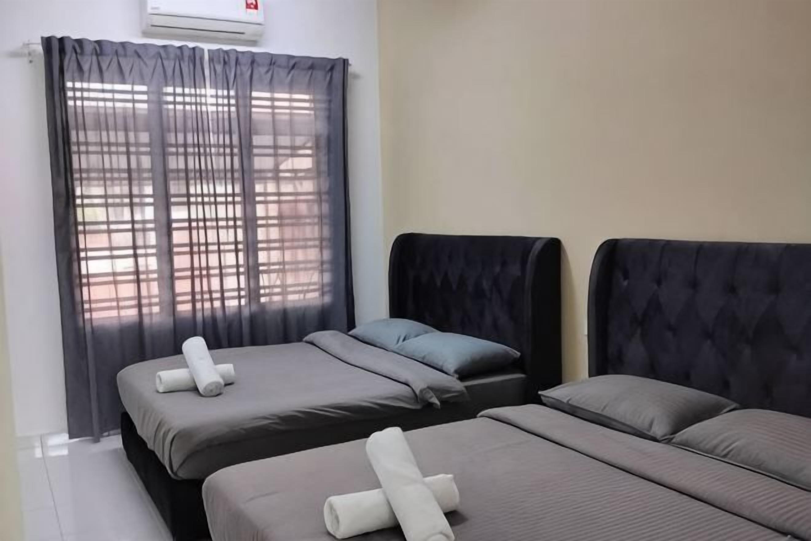 A hotel room with two beds, a window with sheer curtains, and a wall-mounted air conditioner.