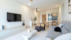 A modern living room with a flat-screen TV, a white coffee table, a grey sofa, and a dining area in the background. - Aradia by FEEL HOME (Kuala Lumpur)