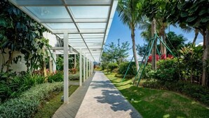 A covered walkway with a glass roof, surrounded by lush greenery and palm trees. - Aradia by FEEL HOME (Kuala Lumpur)