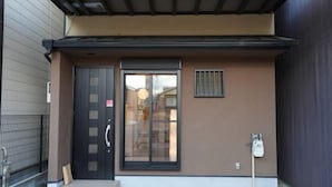 Une entrée d’immeuble avec une porte noire, une porte coulissante en verre et une petite fenêtre.