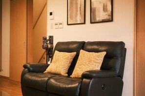 A black leather reclining chair with patterned cushions in a room with a wooden floor and a staircase in the background. - Kyoto Guesthouse（Gojo） (Kyoto)