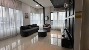 A modern living room with a sofa, armchair, and coffee table, large windows with sheer curtains, a flat-screen TV, and a wall-mounted air conditioning unit. - ARTE@AMPANG (Ampang)