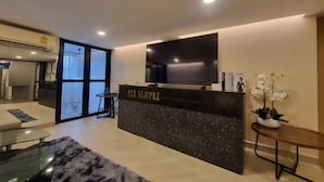 A modern hotel reception area with a flat-screen TV, a reception desk labeled "PER SEMPRE," and a potted orchid. - Oliver's House in Kaset (Bangkok)